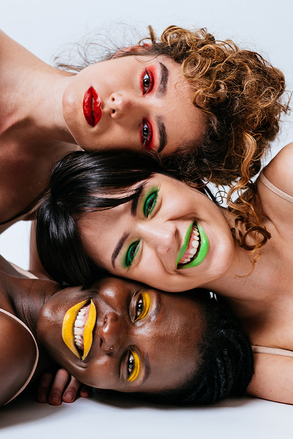 Three women with bold colourful make-up resting their heads together