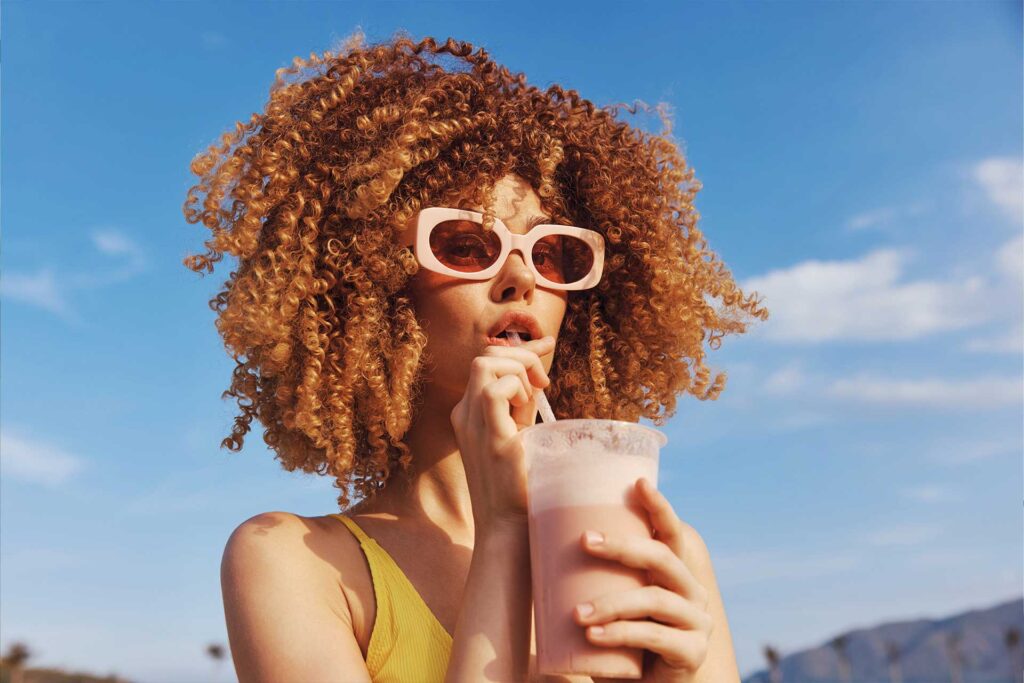 Woman with curly hair sipping a drink under a blue sky